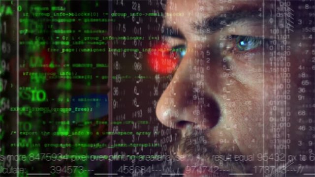 Male hacker working on a computer while green code characters reflect on his face in a dark office room