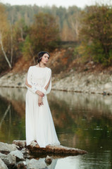 Fototapeta na wymiar A girl in a white dress on the shore of a pond