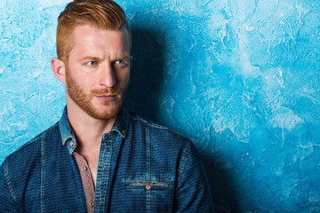 Handsome male model with red hair posing over bright blue background. Studio shot. © alesgon