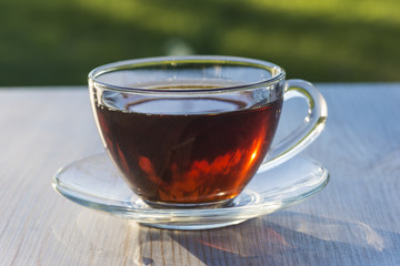 tea time/transparent sunny cup of tea on light wooden table outdtoors