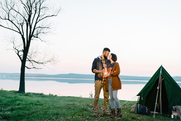 Naklejka na ściany i meble Man and woman lovers hold a flashlight at dawn near the lake