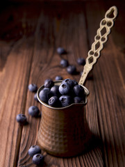 Blueberries in old copper coffee pot on brown wooden surface with space for text