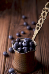 Blueberries in old copper coffee pot on brown wooden surface with space for text