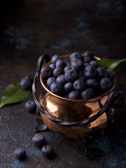 Blueberries and leaves in old copper bowl on dark blue concrete surface with spacer for text. Dark photography