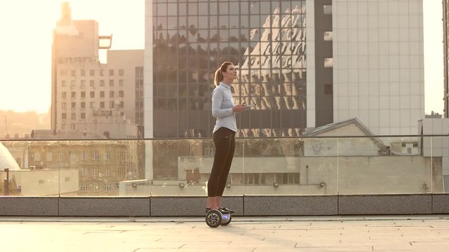 Woman On City Background, Slow-mo. Person On Hoverboard Holding Tablet.