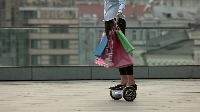 Woman on hoverboard, slow-mo. Female holding bright shopping bags.