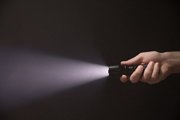 Male hand holding a led flashlight with a wide white beam on a black background, leaving the right side of the frame - obrazy, fototapety, plakaty