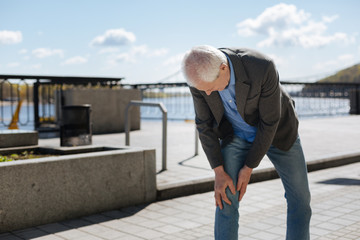 Aging man having pain in his knee on the promenade