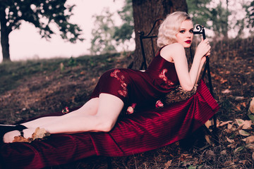 Beautiful and elegant blonde woman with red lips and hair waves wearing wine red nightie posing on...