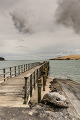 Bay of Islands, New Zealand - March 7, 2017: Exit to Tasman Sea from Hokianga Harbour shows large dune and pier pointing at entrance all under heavy cloudscape because of approaching cyclone. © Klodien