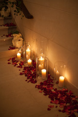 Candle surrounded by red rose petals with dreamy reflection