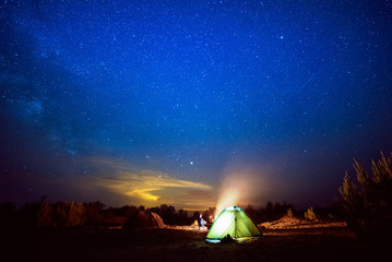 Fototapeta na wymiar Camping fire under the amazing blue starry sky with a lot of shining stars and clouds. Travel recreational outdoor activity concept.