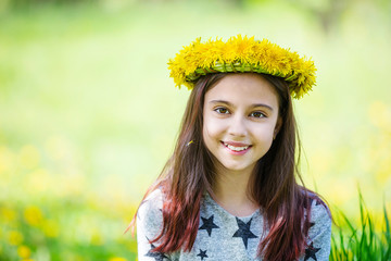 Cute young girl wearing wreath of dandelions and smiling