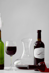 Table with wineglass and bottles of red wine on light background