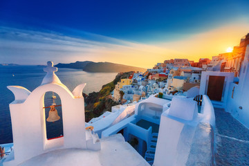 Classical view at sunset over chapel in Oia (Ia) village on Santorini volcano island in Greece. Breathtaking epic sunset scenery. Popular travel tourist destination for romantic trip.