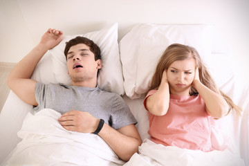 Young irritated woman lying in bed with snoring husband at home