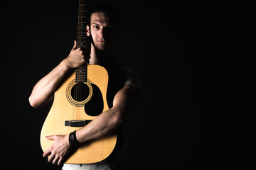 Obraz premium Guitarist, music. A young man stands with an acoustic guitar on a black isolated background. Horizontal frame