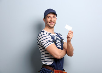Handsome worker with business card on light background