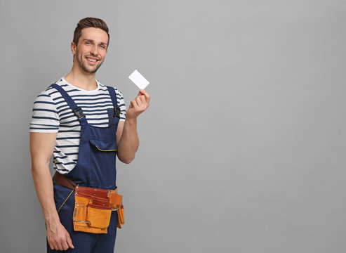 Handsome worker with business card on grey background
