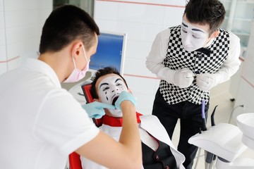 The clown or mime is sitting in the dental chair. The dentist treats the tooth to the patient.