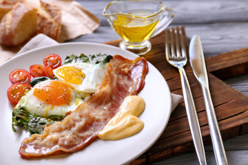 Plate with tasty eggs, spinach and bacon on wooden table