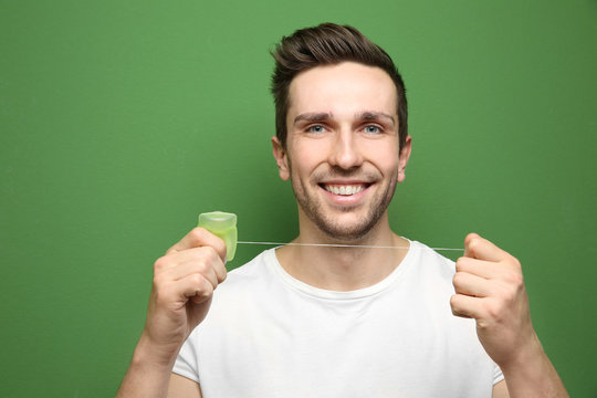 Young handsome man using dental floss on color background