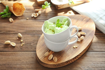 Cups with delicious pistachio ice cream on wooden board