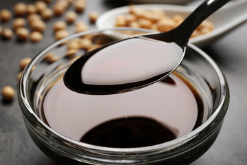 Bowl with tasty soy sauce and spoon on table, closeup
