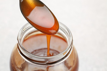 Jar with tasty caramel sauce and spoon on light background, closeup