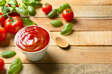 Delicious ketchup with basil and tomatoes on wooden background