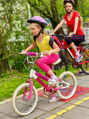 Fototapeta premium Bicycle path and sign with children. Girls wearing helmet with rucksack ciclyng ride. Kids are on yellow bike lane. Alternative to urban transport. Sisters compete in speed for cycling.