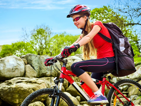 Woman on bicycle ride mountain. Girl traveling in summer park. Early morning with blue sky and clouds. Cycling person with rucksack. Sport trip is good for health. Girl is exploring new terrain .