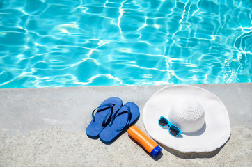 Summer background with hat, sunscreen, flip flops and sunglasses near the pool