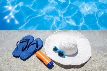 Summer background with hat, sunscreen, flip flops and sunglasses near the pool