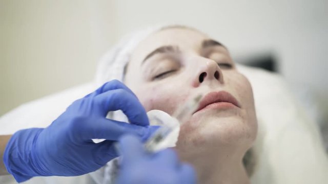 Close up of a cosmetician doing shots near woman s mouth and wiping face with a cotton pad. Handheld real time close up shot