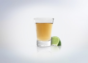 Gold shot of tequila. Alcoholic distilled beverage with slice of lemon / lime on the side. Isolated...