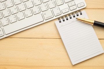 top view. keyboard,pen and small empty notebook paper. both putting on wooden are background. this image for business,education and technology concept
