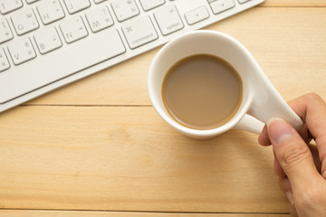 top view. hand of young woman holding coffee cup and have keyboard putting beside it. wooden are background. this image business,beverage and technology concept