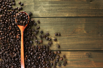 Coffee beans on spoon and wooden background.