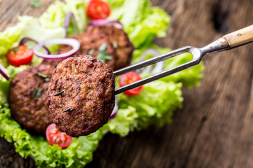 Beef Burgers meatballs cutlets with lettuce salad tomato onion on wooden board.
