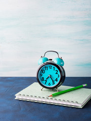 Alarm clock and businessman's accessories on blue background. Office manager morning concept with tie, notebook, stationery