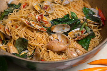Stir fried Clams and Spaghetti with chili paste in the pan on table in the kitchen / Still life image and Selective focus .