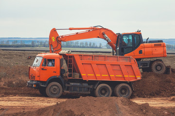 Red wxcavator loading dumper truck at construction of the road