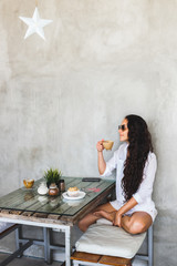 Young brunette woman drink coffee in modern loft cafe with cement walls and textured wooden table. Happy and smile, breakfast with muffin