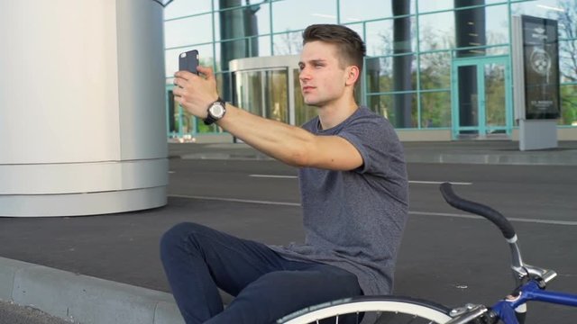 Young man sitting on the border and making a selfshot in front of a building