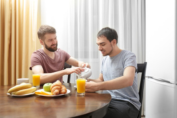 Happy gay couple having breakfast in kitchen