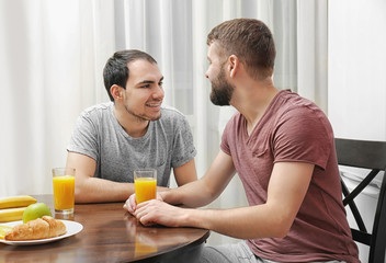 Happy gay couple having breakfast in kitchen