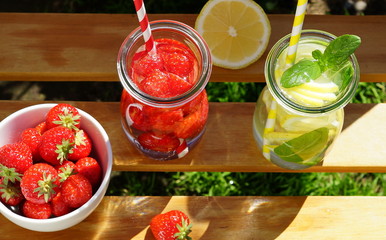Detox water with strawberries and lemon on a wooden background in the garden.top view
