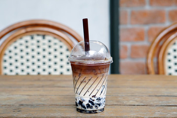 Iced Latte (cold brew) with glass jelly - A Plastic Glass of iced coffee with milk on Wooden table and blurred background, Selective Focus.