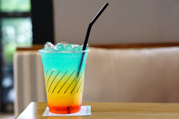 Colorful Cocktail or Tropical Mocktail - Plastic glass of Energy Drink with lemonade, orange juice and watermelon syrup on wooden table and on blurred background, Copy Space.